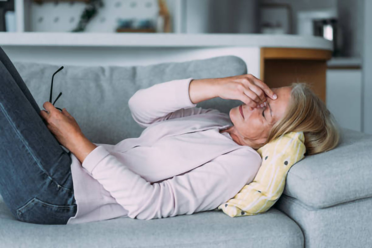 Woman lying on a couch holding her head, showing signs of fatigue, possibly related to stress or adrenal fatigue.